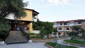 Una entrada de hotel con una escalinata de piedra, un edificio amarillo y un jardín ajardinado.