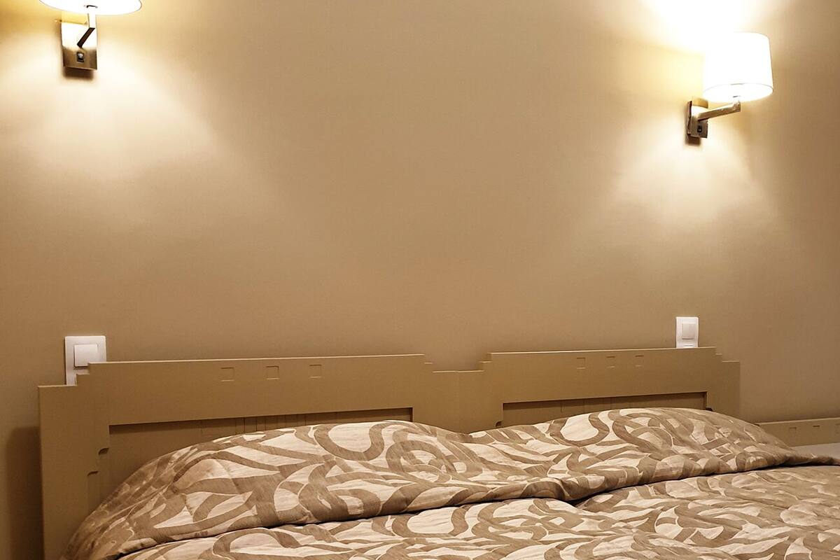 A hotel room with a bed, two wall-mounted lights, and a headboard.