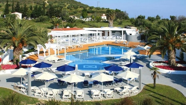 Área de piscina en un resort con tumbonas y sombrillas, rodeada de palmeras y una colina al fondo.