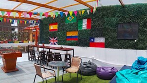 A rooftop bar with a foosball table, outdoor seating, and a wall decorated with various national flags. - Dragonfly Hostels Miraflores (Lima)