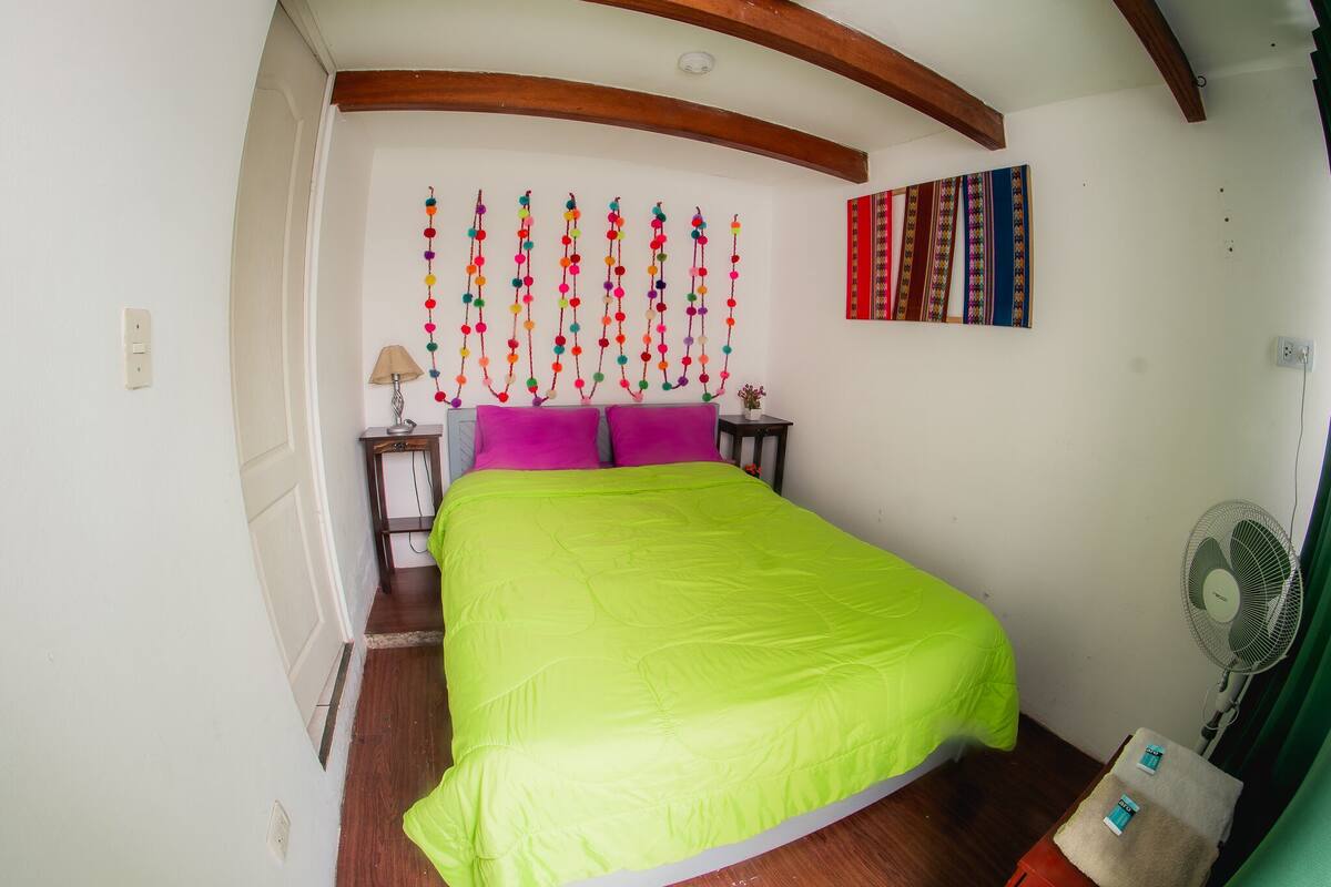 Une chambre à coucher avec un lit, une décoration murale, un ventilateur et une petite table.