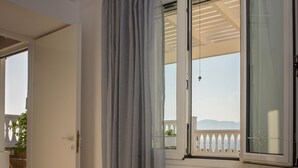 A hotel room with a bed, a window with curtains, an air conditioning unit, and a view of the outdoors.
