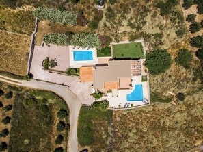 An aerial view of a property with two swimming pools, a large lawn, and a paved driveway.
