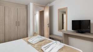 Hotellihuone, jossa on sänky, televisio, puinen vaatekaappi ja peili.