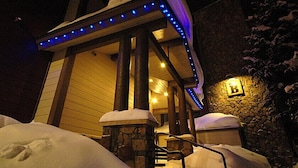 A snow-covered building with a stone entrance and a blue-lit awning. - Park Place Condos by CRMR (Breckenridge)