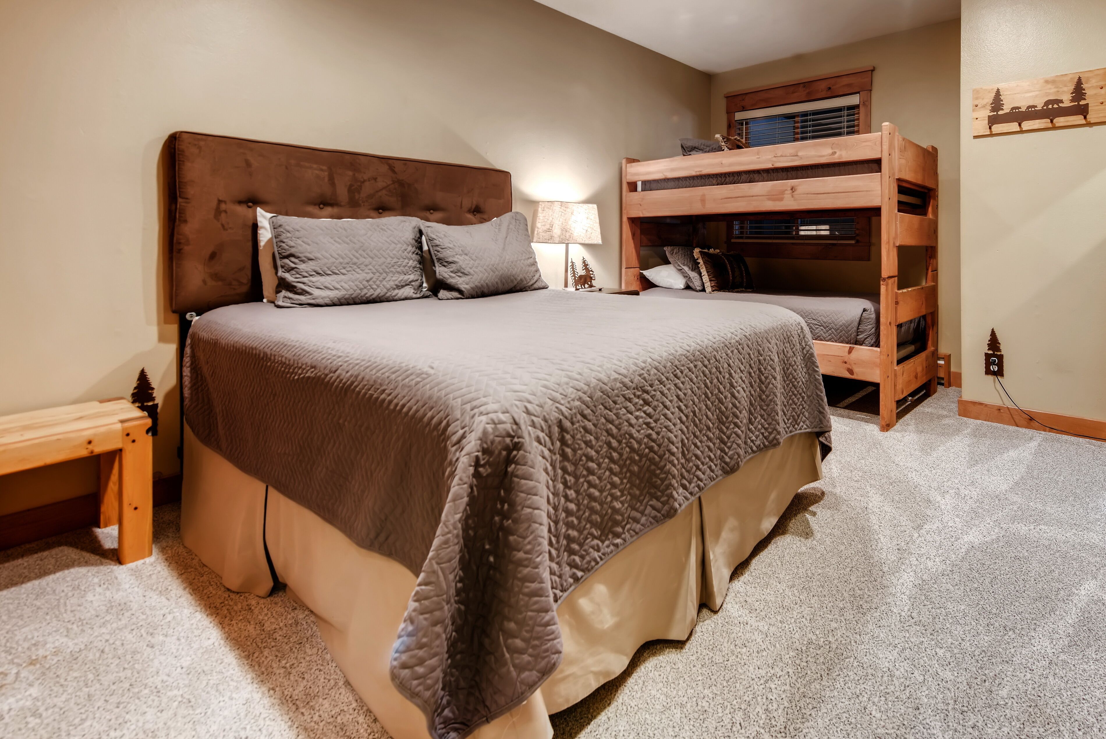 A bedroom with a large bed, a wooden bunk bed, a bedside table, and a lamp.
