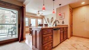 A spacious kitchen with a large island, wooden cabinets, and a view to the outside. - Park Place Condos by CRMR (Breckenridge)