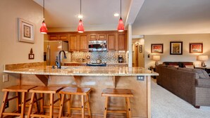 A kitchen with a large island, wooden stools, and a refrigerator. - Park Place Condos by CRMR (Breckenridge)