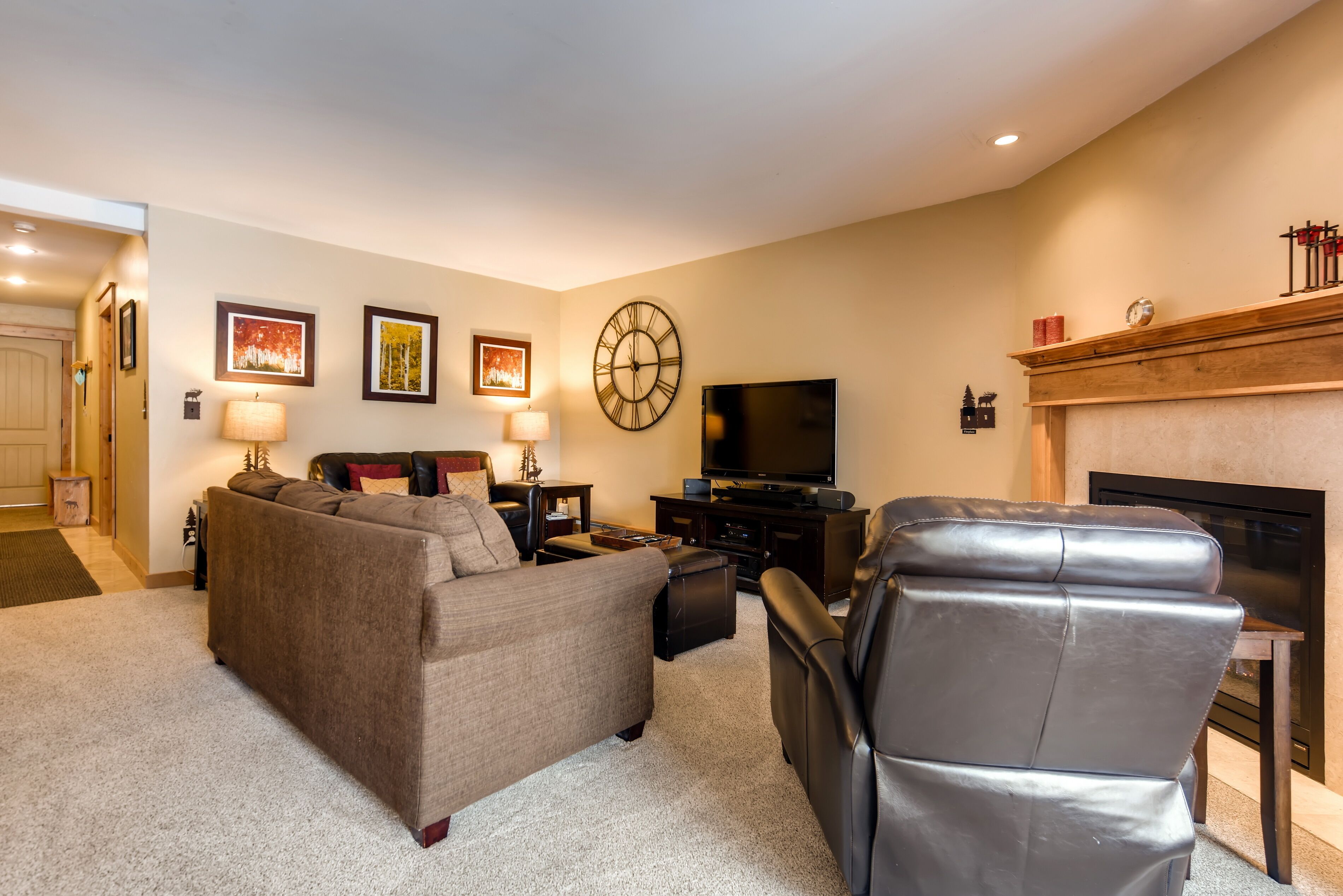 Una sala de estar con sofá, sillón de cuero, televisor, chimenea y cuadros en la pared.