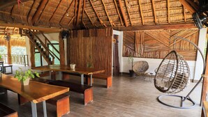 Une pièce spacieuse avec un plancher en bois, un toit de chaume et un fauteuil suspendu.