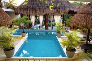 A pool area with a clear blue pool, surrounded by potted plants and thatched umbrellas. - Diosa del Agua Bacalar (Bacalar)