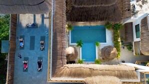 Vue aérienne d’un complexe hôtelier doté d’une piscine centrale, de plusieurs tapis de yoga et de parasols en chaume.