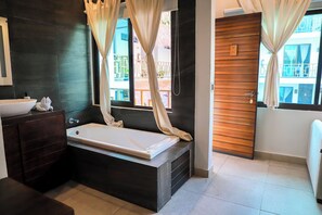 A modern bathroom with a bathtub, dark tiles, a wooden door, and a window with curtains. - Diosa del Agua Bacalar (Bacalar)