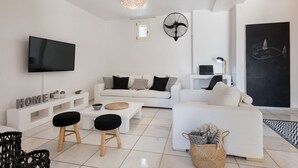 En moderne stue med et fladskærms-tv, hvide sofaer, et sofabord og en stor ventilator.