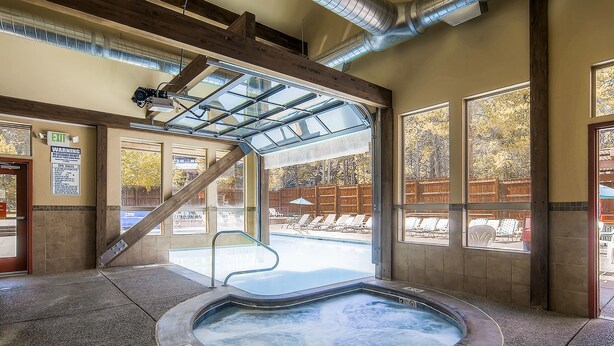 A hot tub area with a glass ceiling, a pool visible through the glass, and a wooden deck outside.