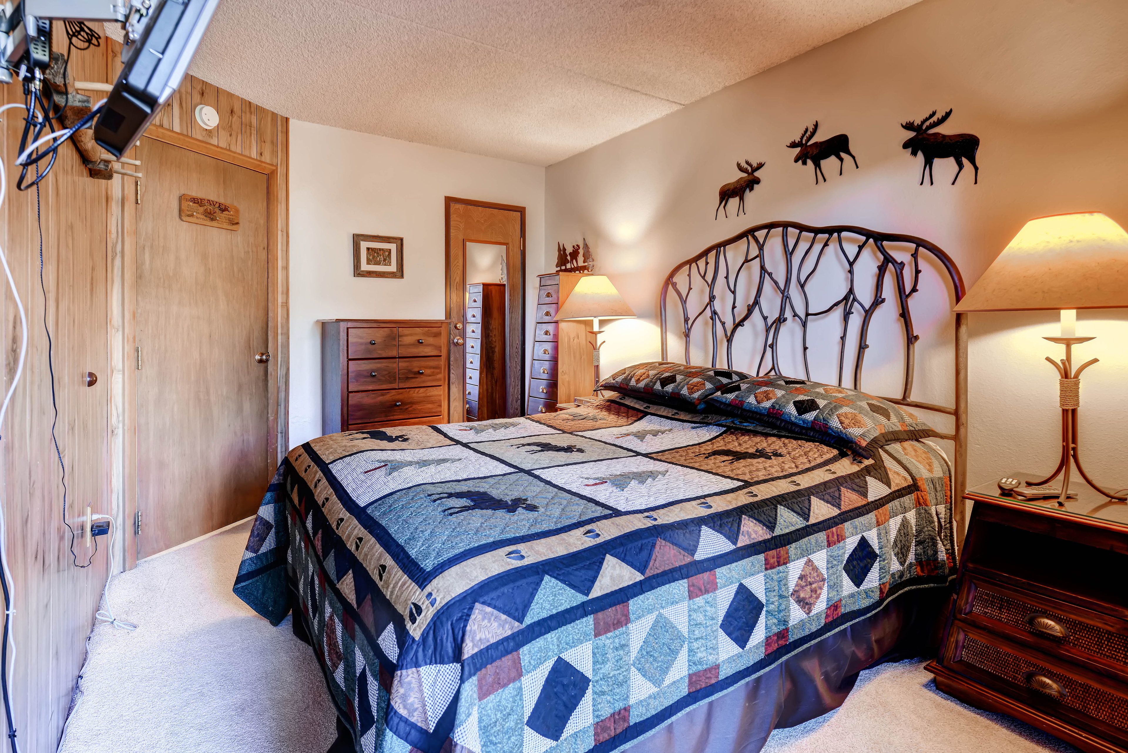 A bedroom with a large bed, wooden wardrobe, and a wall with moose decorations.