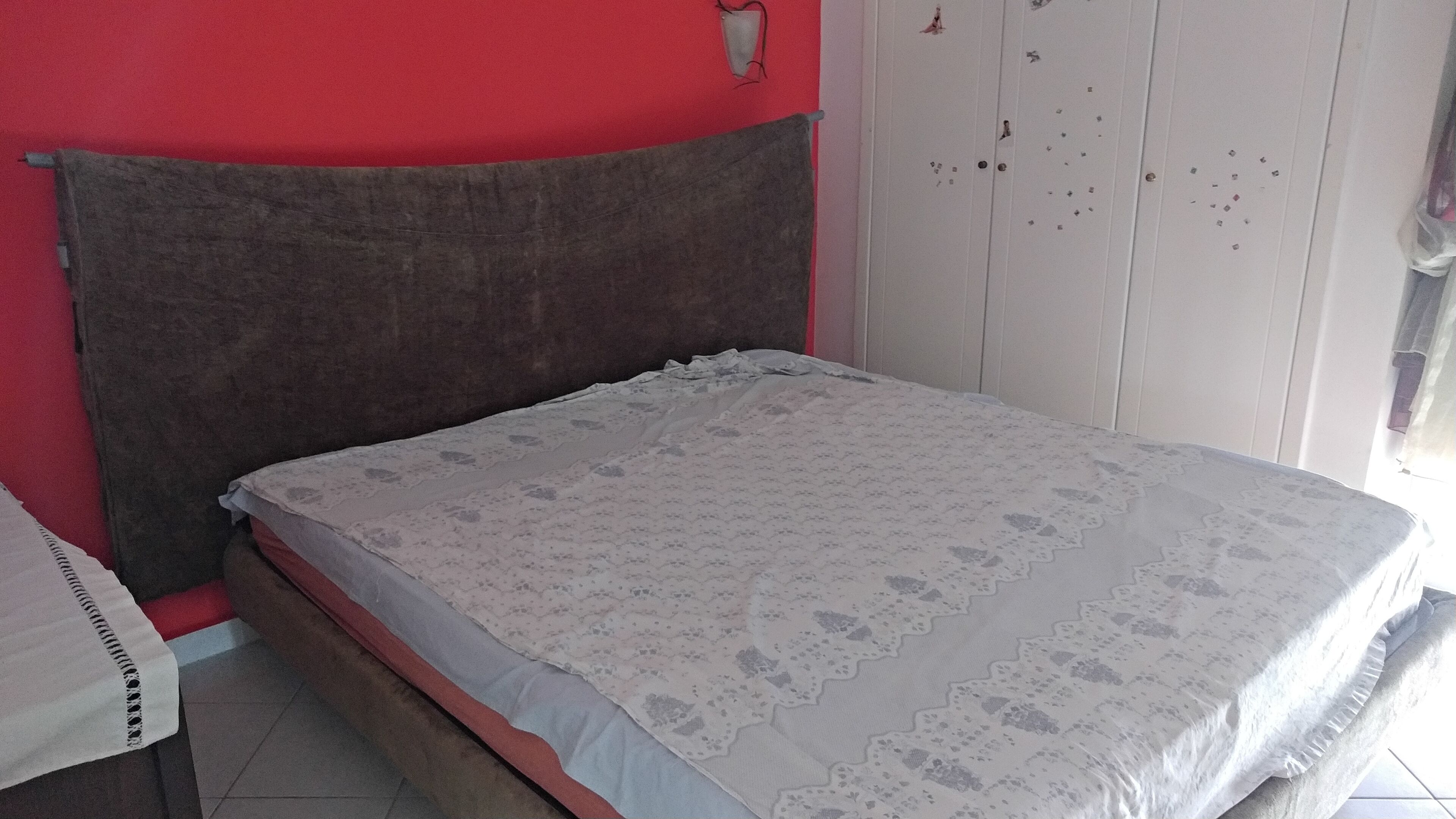 A room with a bed, a red wall, and a white wardrobe.