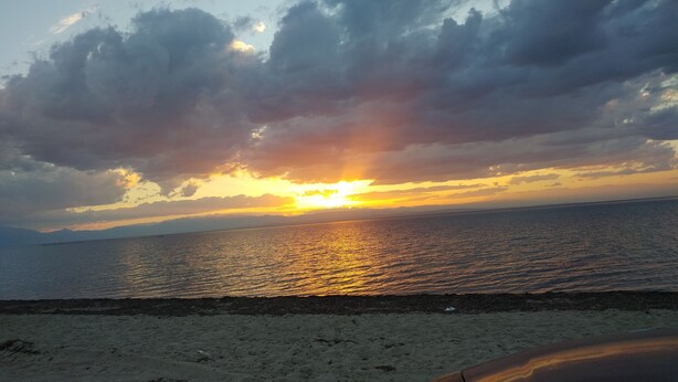 Una spiaggia con un tramonto sull'oceano, cielo sereno e montagne in lontananza.