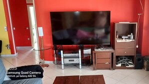 Un soggiorno con una grande televisione a schermo piatto, un mobiletto in legno e un termosifone.