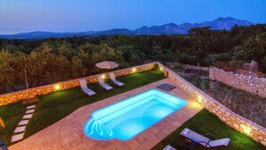 A swimming pool with a stone border, surrounded by a stone wall, and equipped with outdoor lighting. - Green Paradise Luxury Villa In Crete  (Τζαννακιανά)