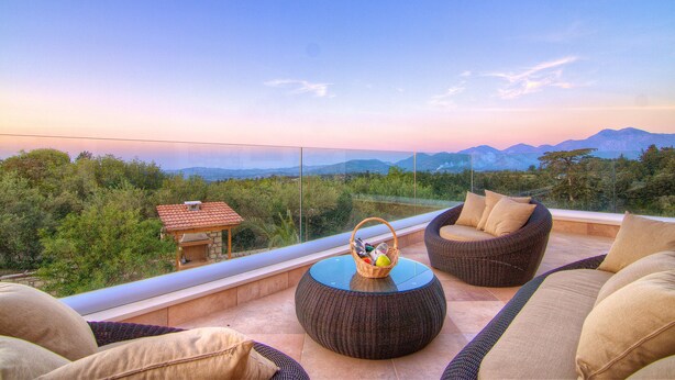 A balcony with wicker furniture, a small table, and a basket of items. - Green Paradise Luxury Villa In Crete  (Τζαννακιανά)