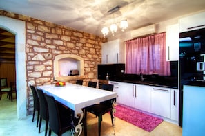 A compact kitchen with a stone wall, white cabinets, a dining table with chairs, and a pink rug.