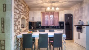 A modern kitchen with stone walls, a dining table with chairs, and a refrigerator. - Green Paradise Luxury Villa In Crete  (Τζαννακιανά)