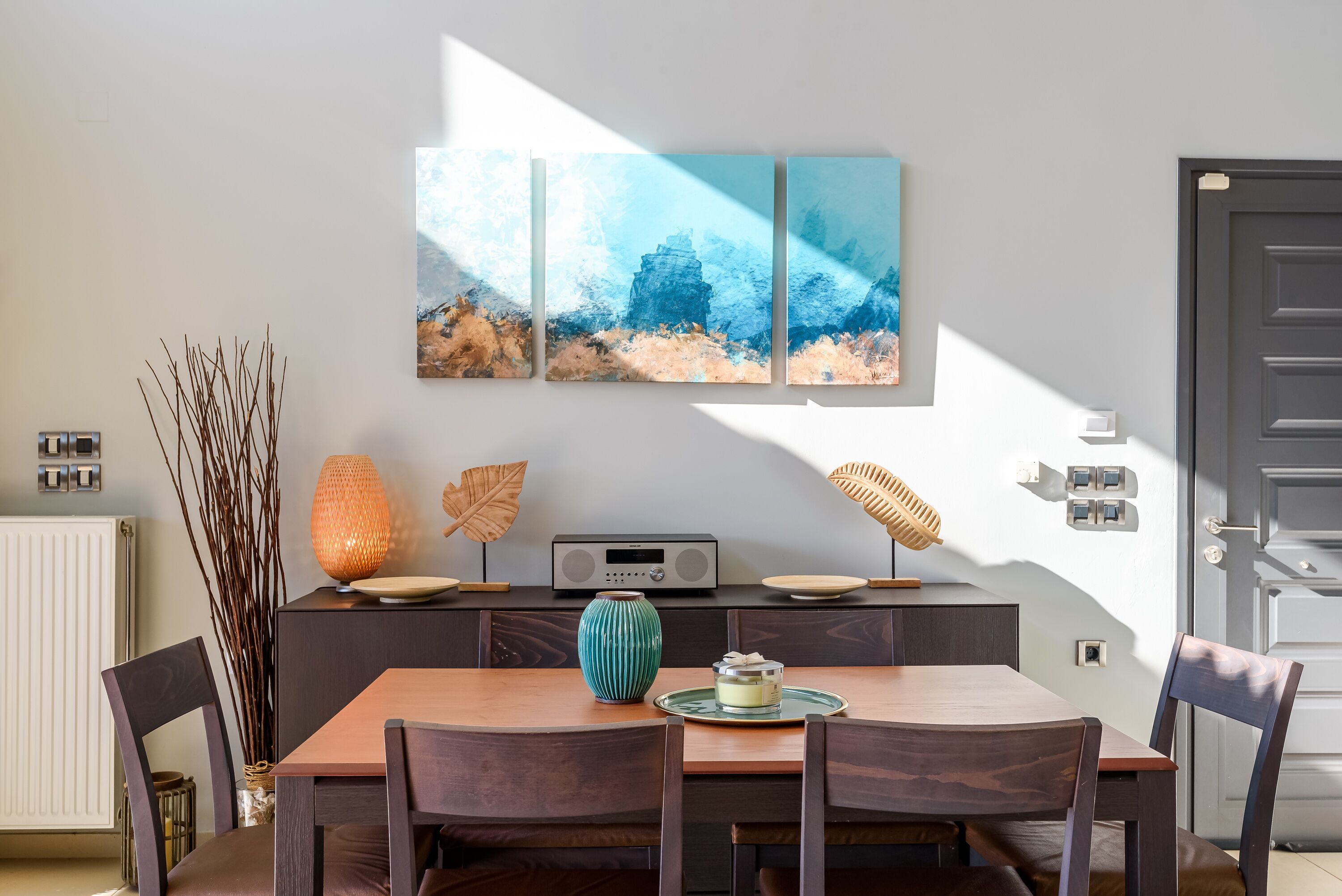 A dining area with a wooden table, chairs, a radio, decorative items, and a wall-mounted painting.