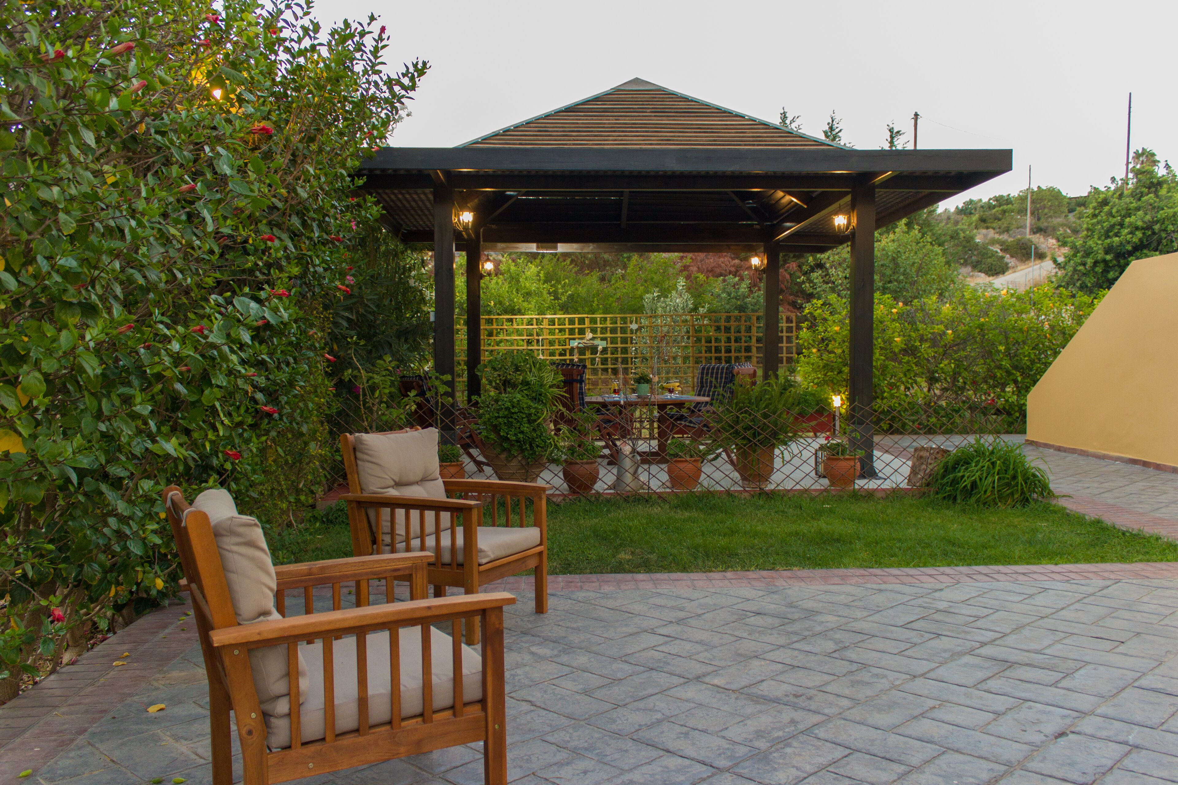A gazebo with a tiled patio, wooden chairs, and potted plants.