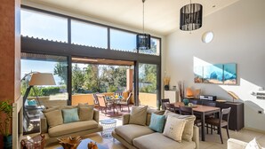 Ein geräumiger Wohnbereich mit Sofa, Couchtisch und Esstisch. Große Fenster bieten einen Ausblick ins Freie.