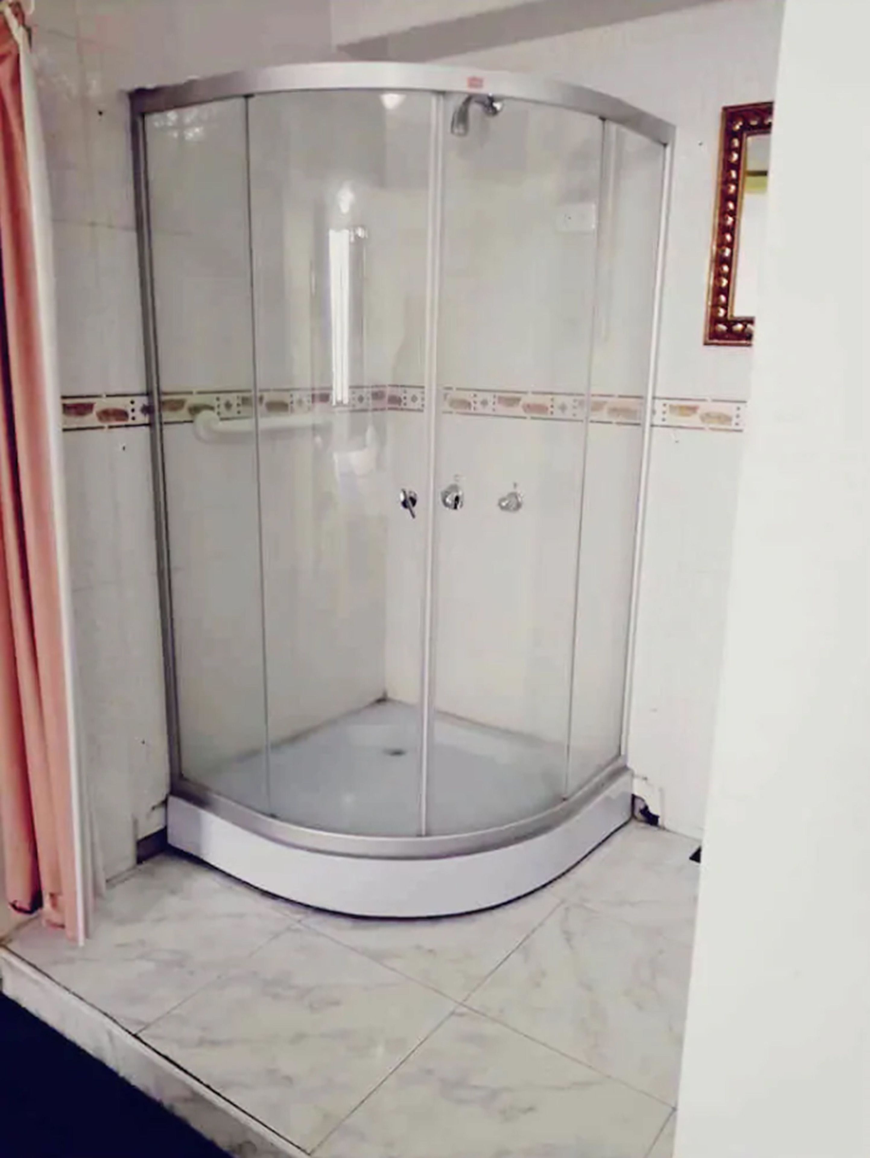 Un espace de douche d’angle doté d’une porte en verre et d’un sol carrelé.