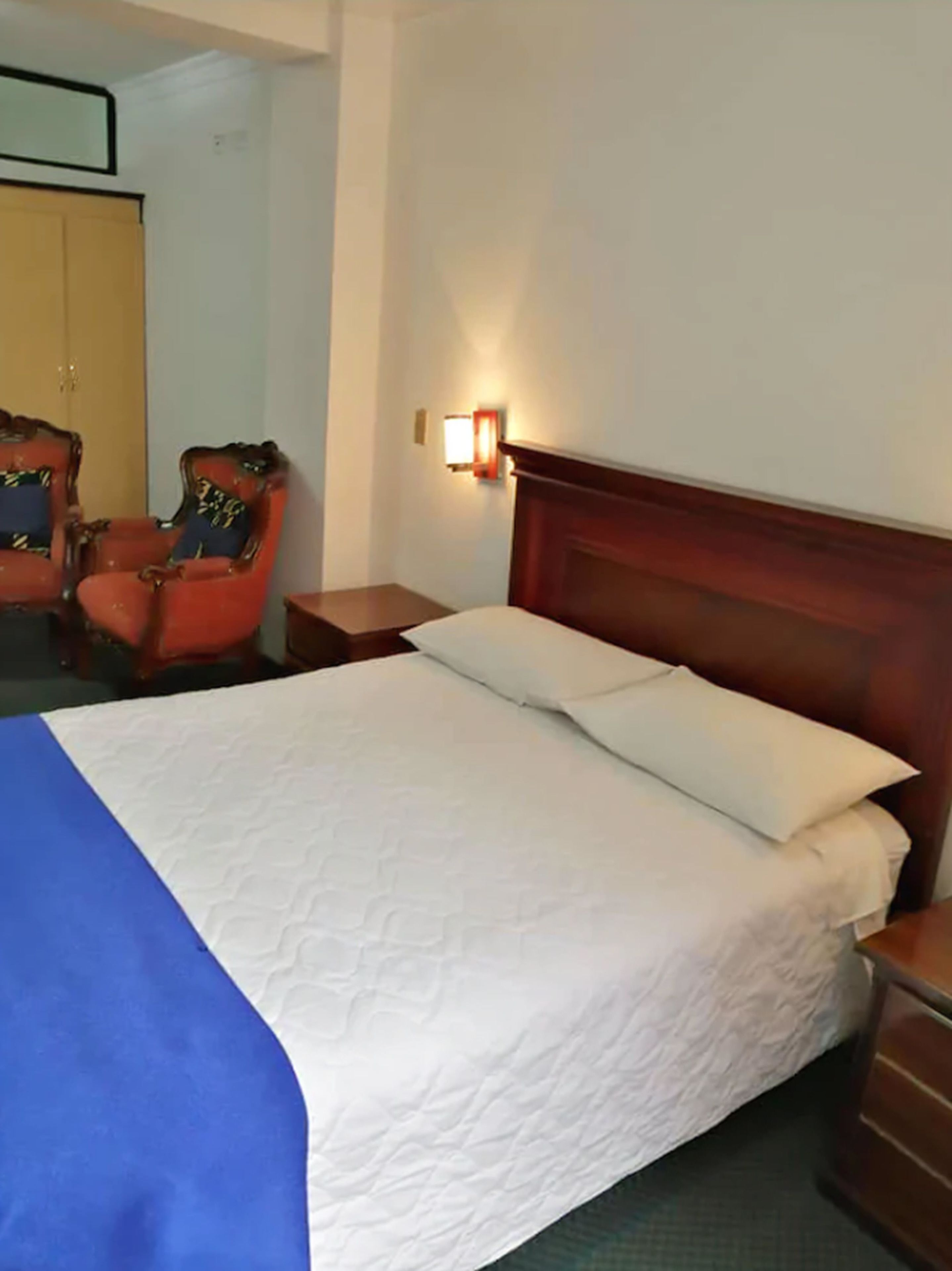 A hotel room with a bed, a nightstand, a lamp, and two chairs.