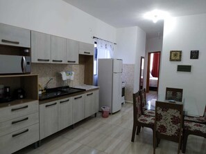 A kitchen with light-colored cabinets, a refrigerator, a sink, and a dining area with a table and chairs.