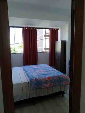 A bedroom with a bed, a wardrobe, and a window with curtains.