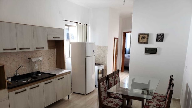 A modern kitchen with a dining area, featuring a glass table and floral chairs, light wooden cabinets, and a refrigerator. - Apartamento Central Setti (Foz do Iguaçu)