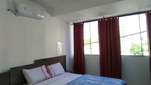 A bedroom with a bed, a window with curtains, and an air conditioning unit on the wall. - Apartamento Central Setti (Foz do Iguaçu)