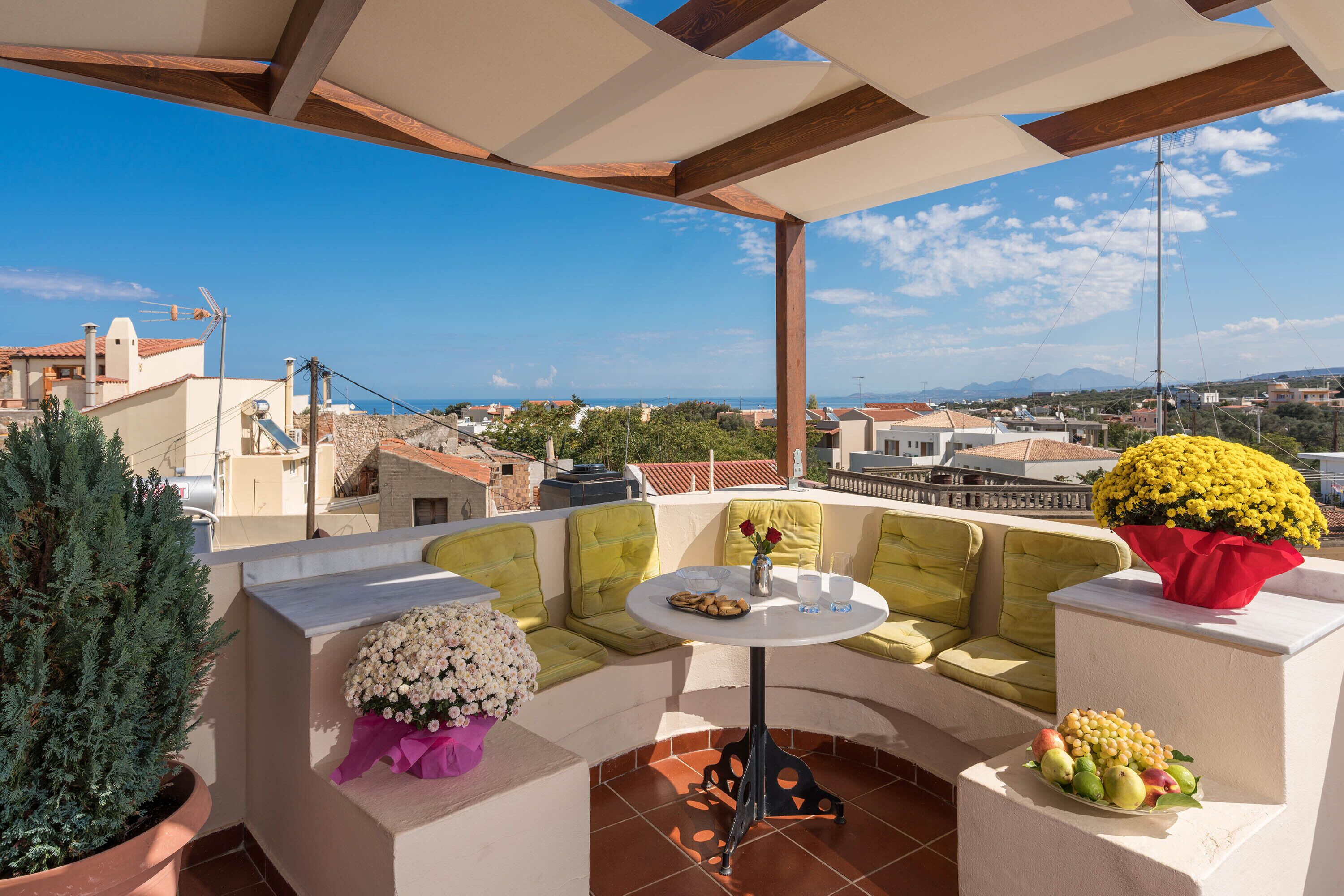 A rooftop terrace with a seating area, a table, and potted plants.