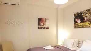 A hotel room with two beds, a chair, a painting, and a wall-mounted rack. - New, large apartm. with private garden, 3' to the sea and 5' to the city centre (Καλαμάτα)