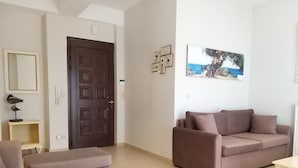 A living room with a brown sofa, a matching armchair, a small table, and a door. - New, large apartm. with private garden, 3' to the sea and 5' to the city centre (Καλαμάτα)