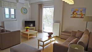 A living room with a sofa, a coffee table, a TV, and a painting on the wall. - New, large apartm. with private garden, 3' to the sea and 5' to the city centre (Καλαμάτα)