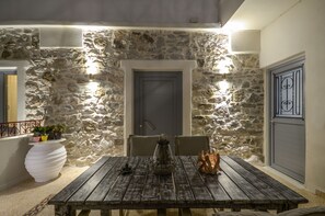 A stone wall exterior with a wooden table and chairs, a door, and a potted plant.