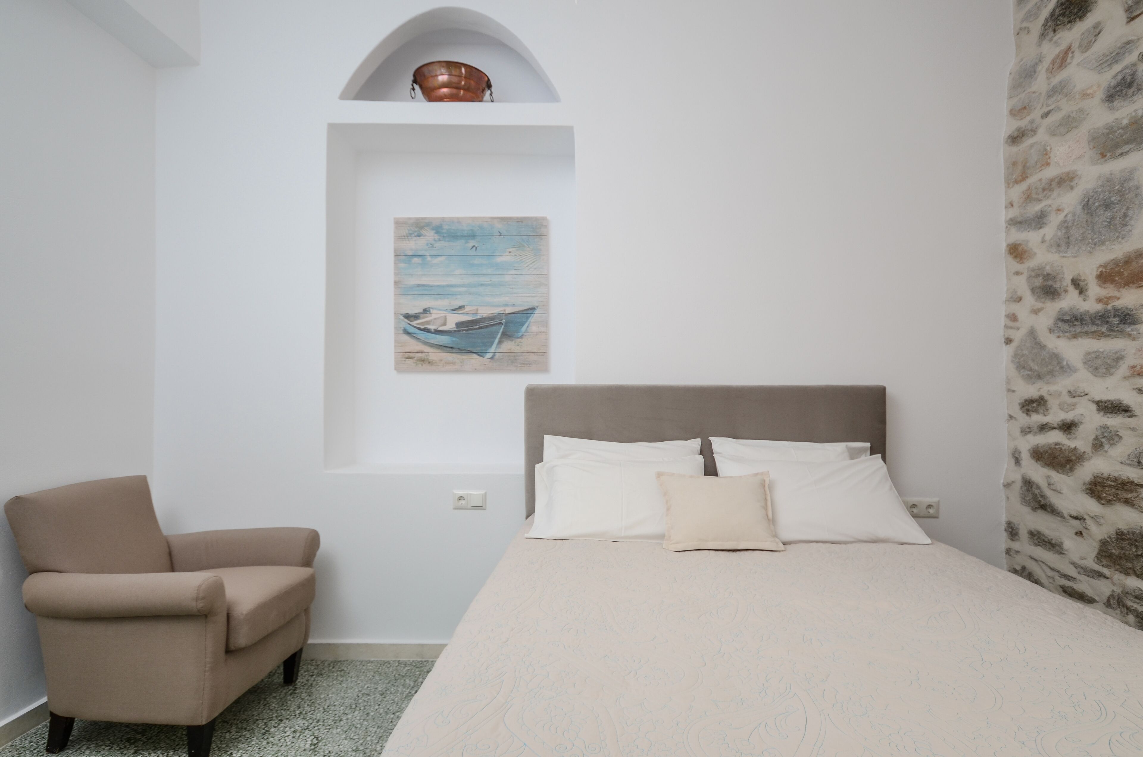 Un dormitorio con una cama, una silla, un cuadro y una pared de piedra.