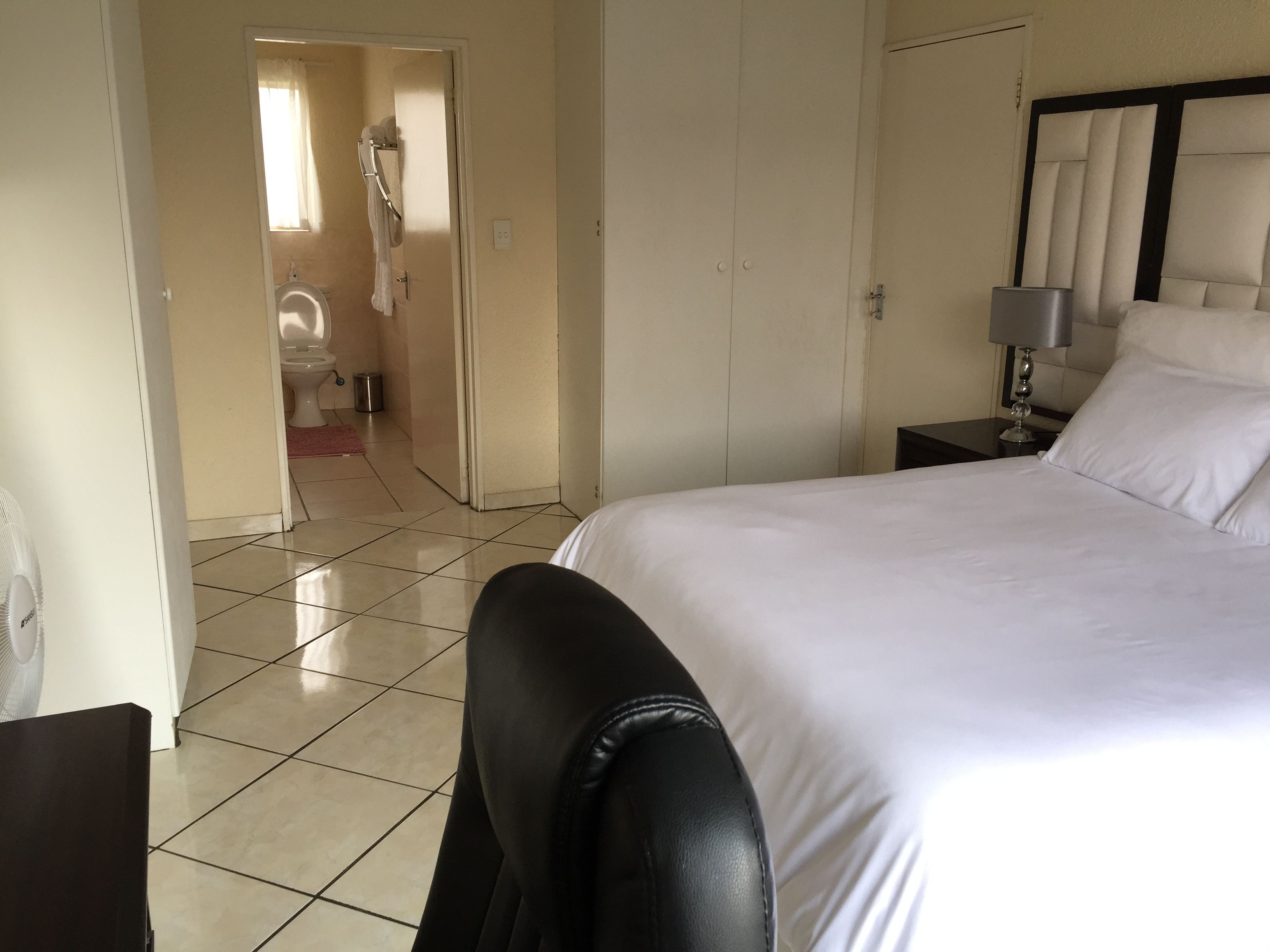 A hotel room with a large bed, a bedside table with a lamp, a chair, and a view of the bathroom.