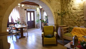 A rustic interior with a dining area, a yellow armchair, a wooden sofa, and a stone wall. - Crete villa Estia (Ρεθυμνο)