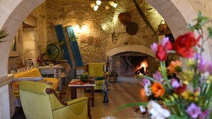 A cozy interior with a stone wall, a fireplace, yellow chairs, and a table with flowers. - Crete villa Estia (Ρεθυμνο)