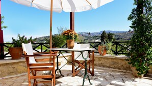 An outdoor patio with a table and chairs, surrounded by potted plants and a view of the hills. - Crete villa Estia (Ρεθυμνο)