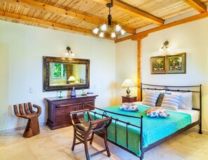 Ein Schlafzimmer mit Holzboden, einem Bett mit grüner Bettdecke, einem Nachttisch mit Lampe, einem Schminktisch, einem Stuhl und einem Spiegel.