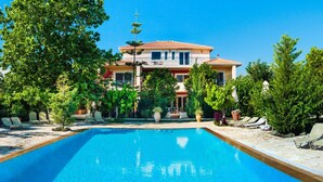 A swimming pool with lounge chairs and a building with a tiled roof in the background. - Top floor suite near to the town and close to the beach (Lefkada)