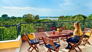 A terrace with a table and chairs, a woman seated, and a view of the sea and greenery. - Top floor suite near to the town and close to the beach (Lefkada)
