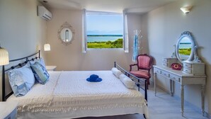 A bedroom with a bed, a chair, a dresser, a mirror, and a window with a view of the sea. - Top floor suite near to the town and close to the beach (Lefkada)
